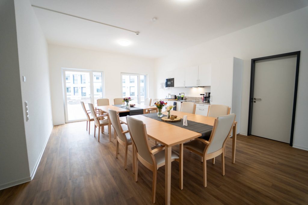Man sieht einen der Essbereiche der Senioren-WG Springbachhöfe Paderborn, mit Wohnküche und Blick auf die begrünte Dachterrasse.